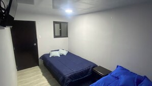 Una habitación pequeña y con poca luz, con dos camas, un escritorio y una puerta.