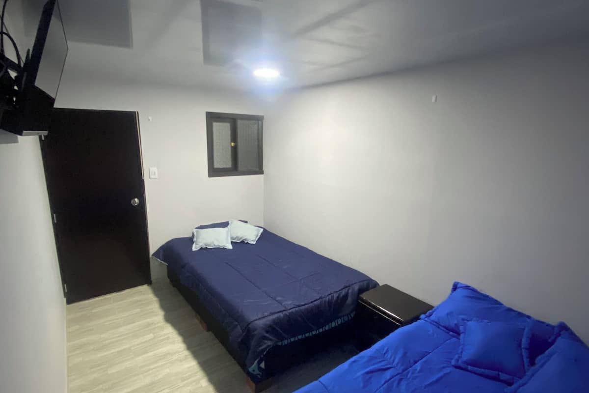 A small, dimly lit room with two beds, a desk, and a door.