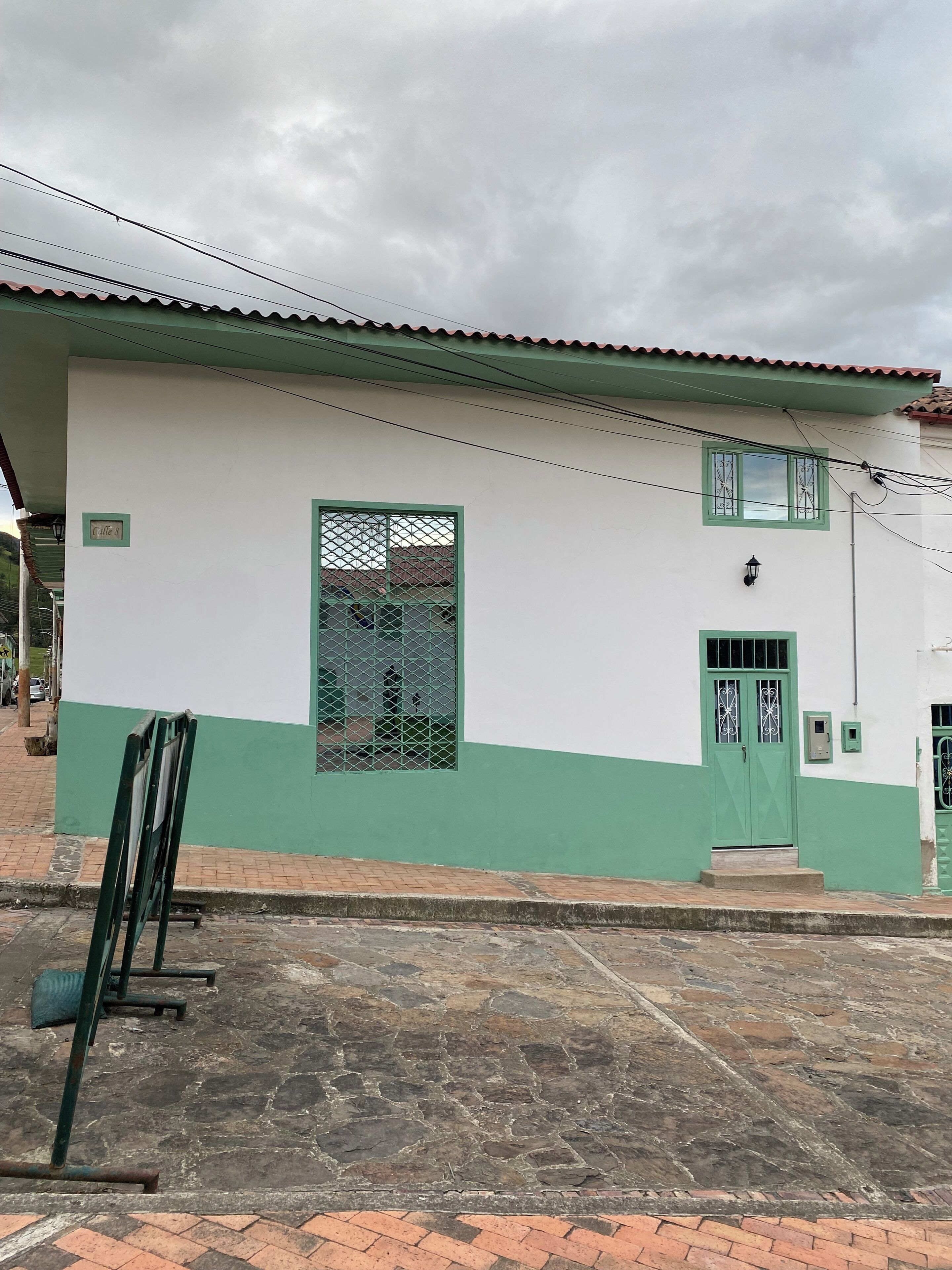 A building with a green and white facade, a metal gate, and a tiled roof.