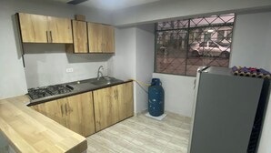 Una cocina con armarios de madera, estufa a gas, refrigerador y cilindro de gas.