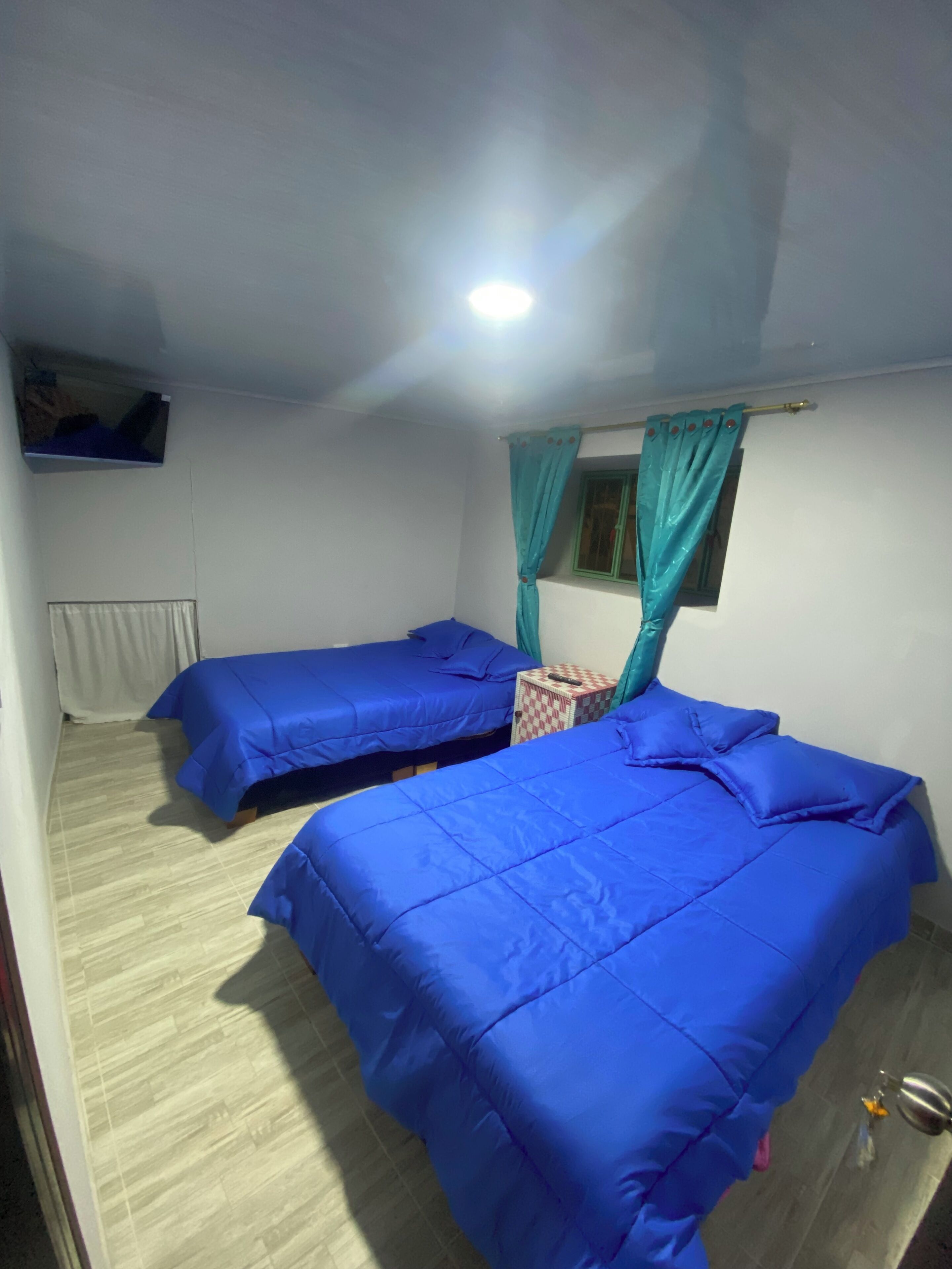 A room with two beds, a small table, a television, and a window with curtains.