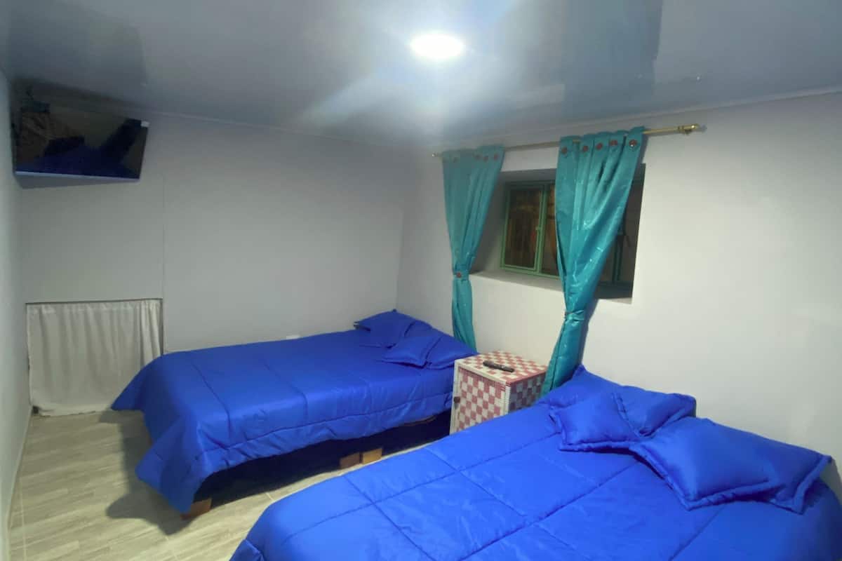 A room with two beds, a small table, and a window with curtains.