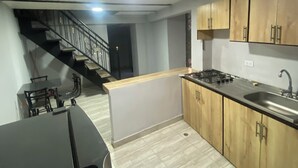 Una cocina moderna con armarios de madera, encimera negra y estufa a gas. Hay un comedor con mesa y sillas, y una escalera que sube a otro nivel.
