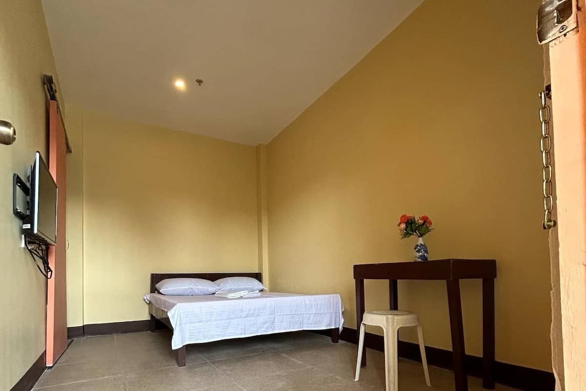 A room with a bed, a small table with a vase, and a television mounted on the wall.
