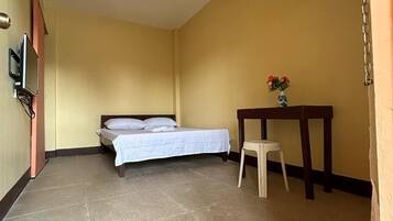 Una habitación con una cama, una mesita con un florero y un televisor montado en la pared.