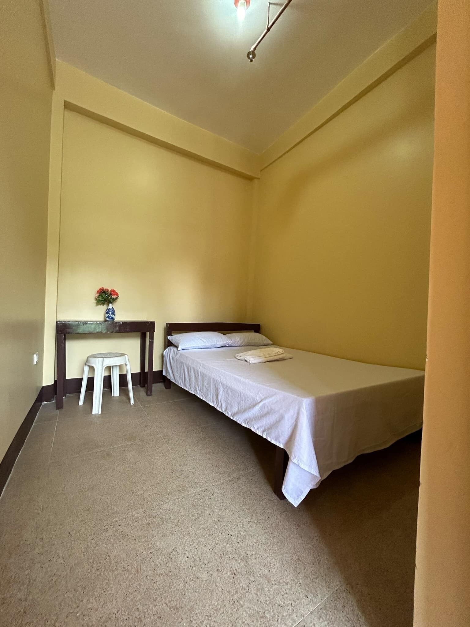 Una habitación pequeña con cama individual, un escritorio de madera y un taburete.