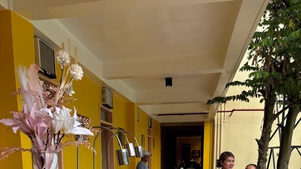 Un buffet est installé avec une longue table recouverte d’une nappe à motifs, entourée de plateaux de service en métal et agrémenté d’un arrangement floral décoratif.