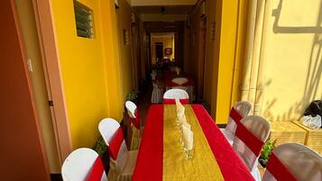 A long dining table with a red and gold table runner, white chairs with red sashes, and a yellow wall in the background.