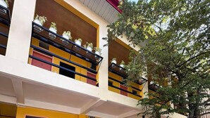 Un immeuble à plusieurs étages avec des portes jaunes et rouges, un escalier et un arbre au premier plan.