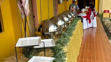 A buffet setup with a long serving table, white tablecloths, and a decorative plant arrangement.