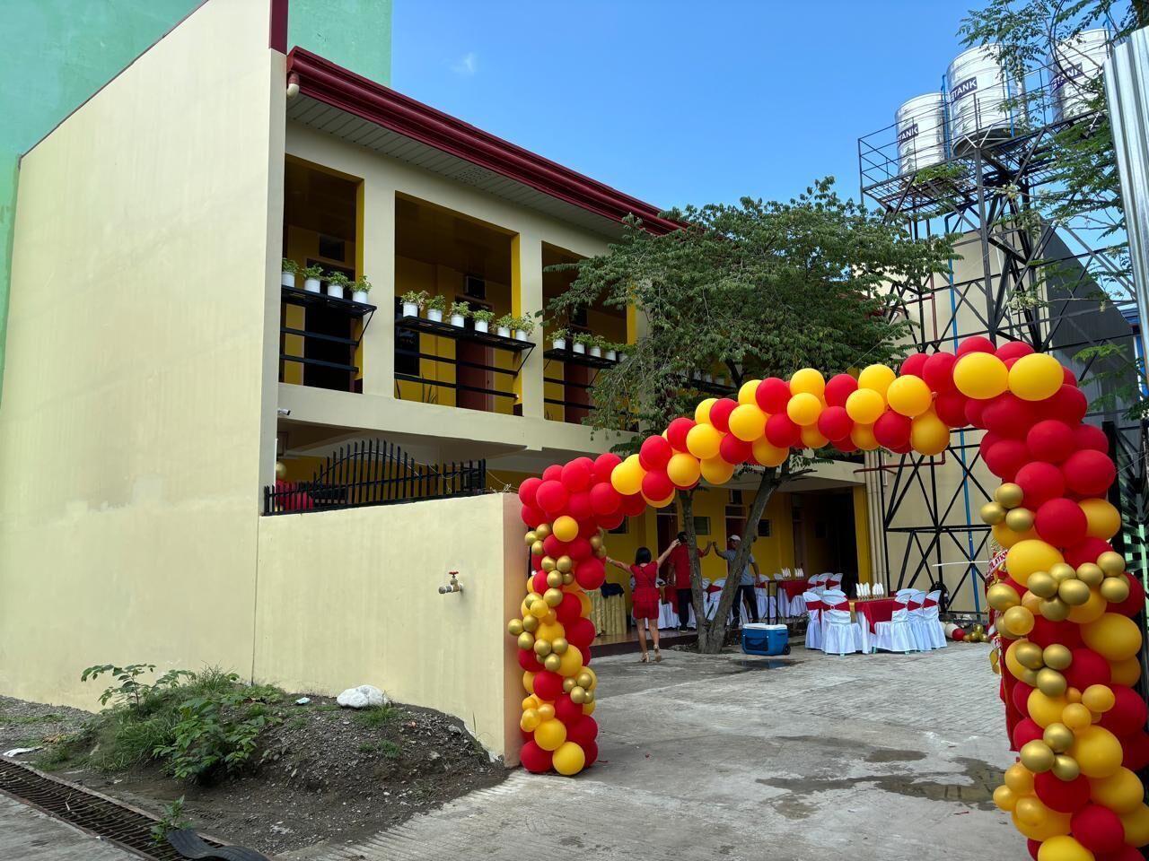 A building with a yellow facade and a red roof, featuring balconies and a gated entrance.