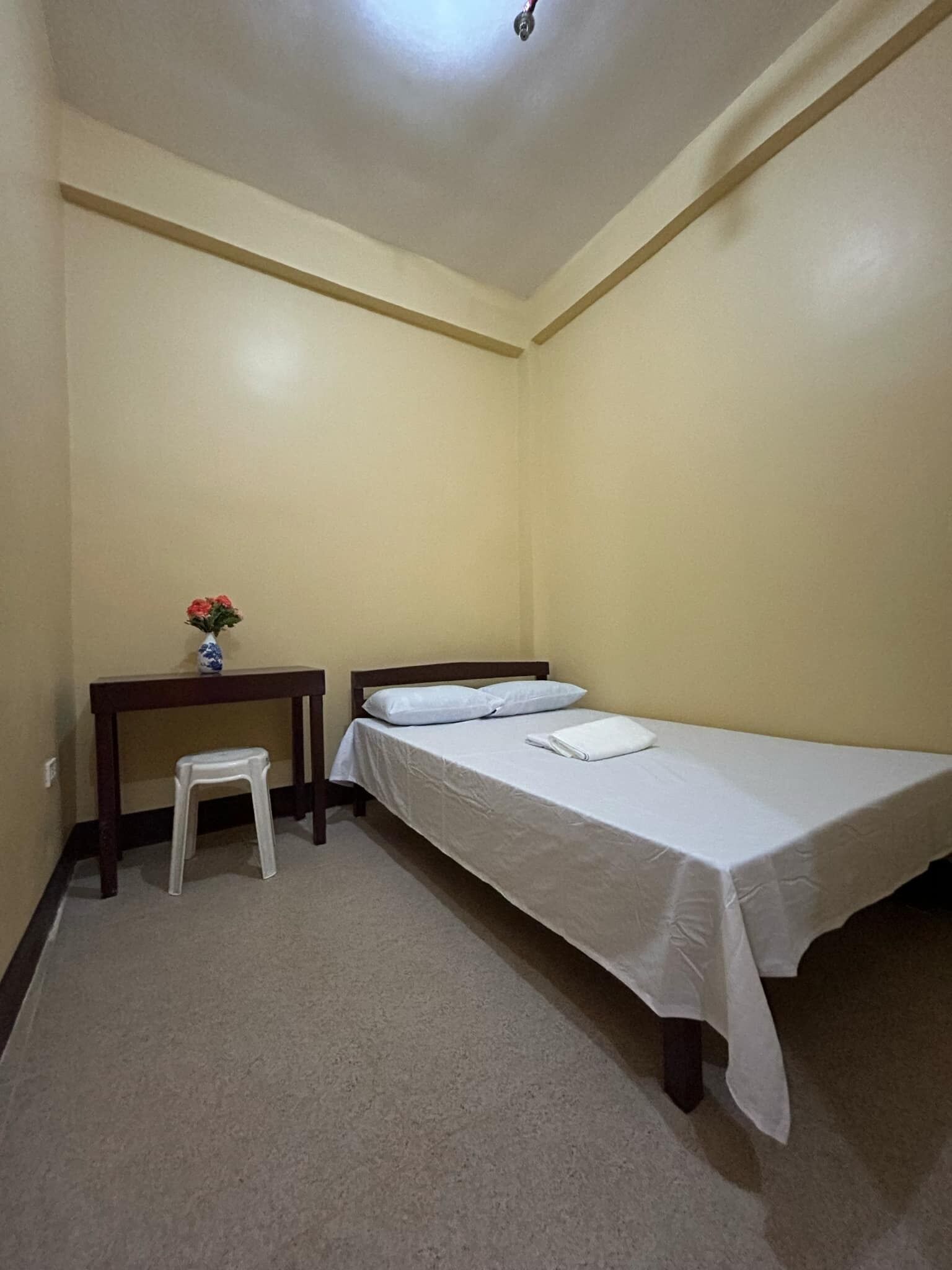 Una habitación pequeña y sencilla con una cama individual, una mesita y un taburete.