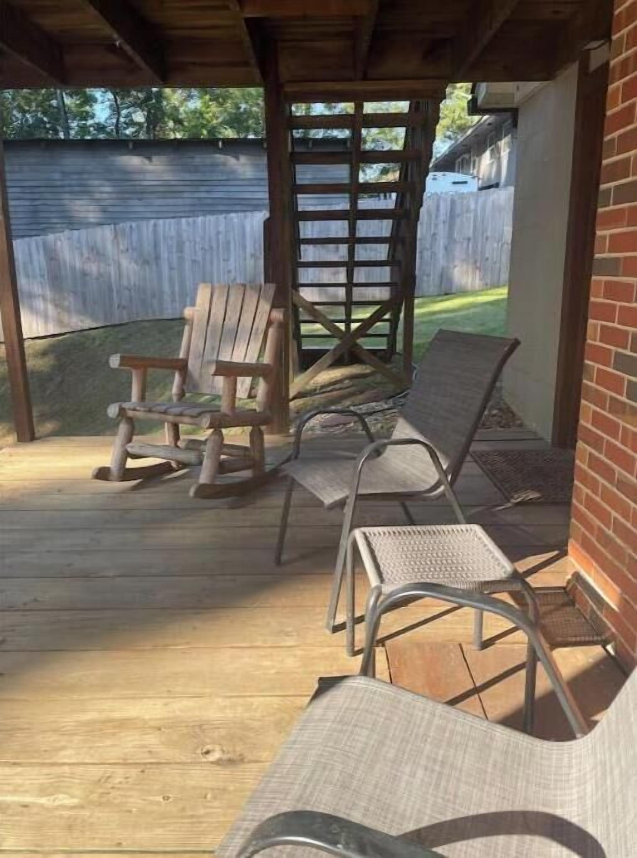 Un patio cubierto con piso de madera, sillas de metal y una silla de madera.