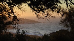 A coastal view with a beach, ocean, and a distant town. - Ikaros Star Hotel (Ikaria)