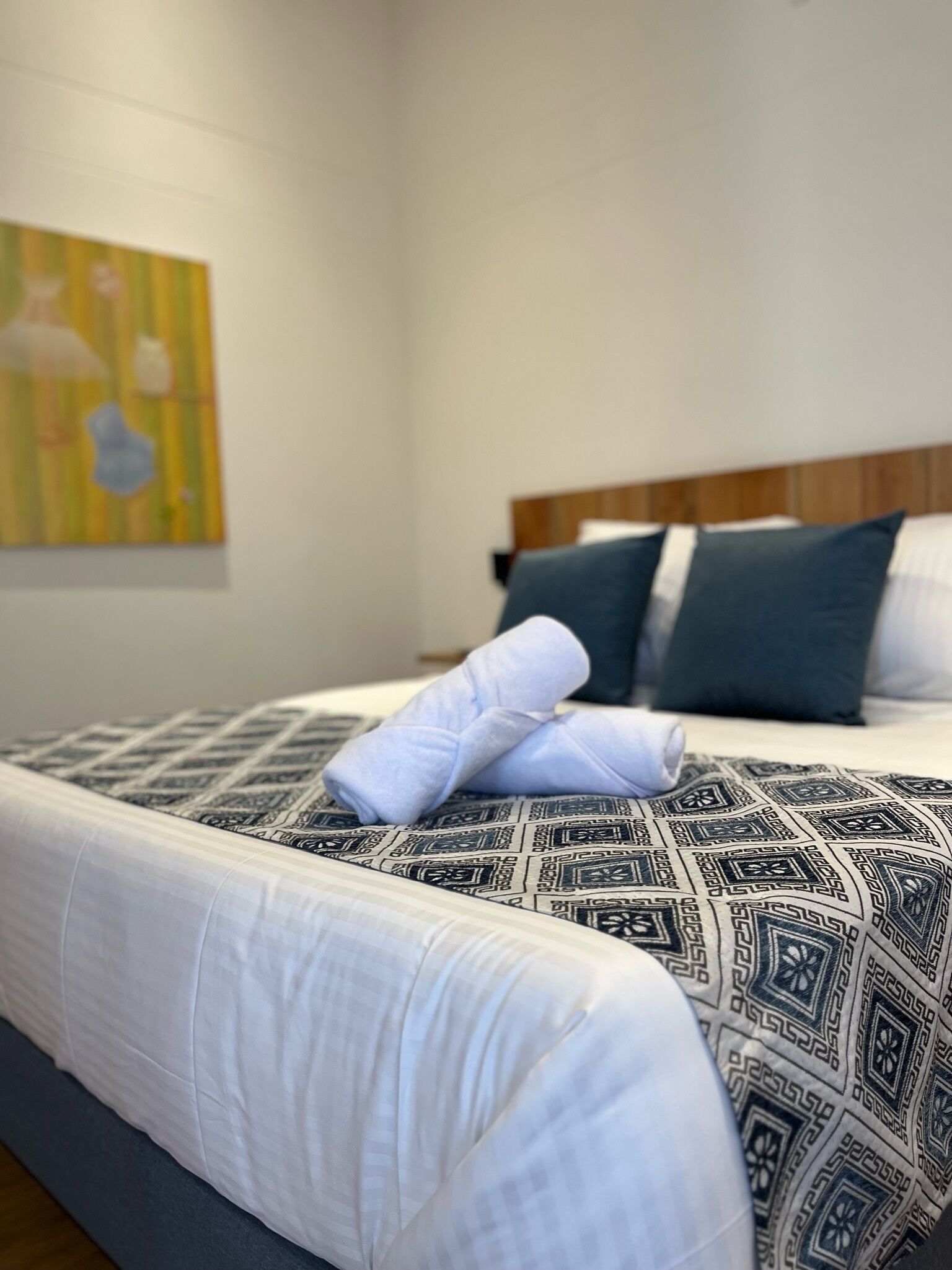 Una cama bien hecha con ropa de cama estampada, un cabecero de madera y una obra de arte en la pared.