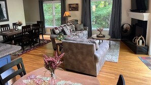 A spacious living room with a fireplace, a dining area, and a large window with curtains. - Helen Haus, Sleeps 10, Fire Pit / Pool Table! Golf (Helen)