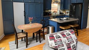 A compact kitchen with dark blue cabinets, a central island, and a dining area with a table and chairs. - Helen Haus, Sleeps 10, Fire Pit / Pool Table! Golf (Helen)