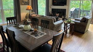 A spacious living room with a dining area, large windows, a fireplace, and a TV mounted on the wall. - Helen Haus, Sleeps 10, Fire Pit / Pool Table! Golf (Helen)