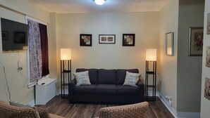 A living room with a dark-colored sofa, two armchairs, a flat-screen TV, and two floor lamps. - Luxury 1 bedroom, 1 Bath apt. in the middle of downtown Detroit w/parking spot!  (Detroit)