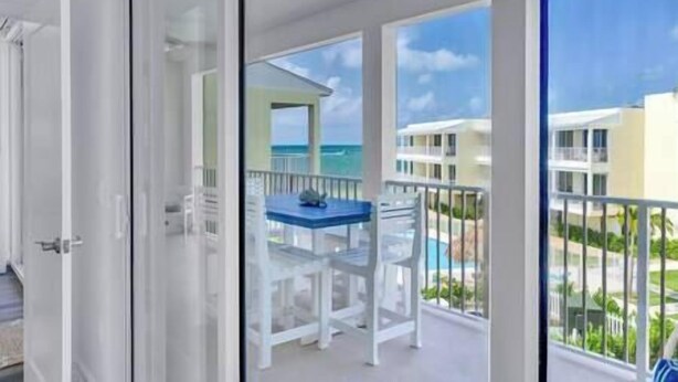 A balcony with a table and chairs, overlooking a pool and buildings.