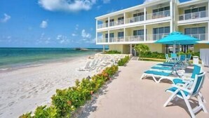 A beachfront hotel with multiple balconies, a pool area with lounge chairs, and a clear view of the ocean.