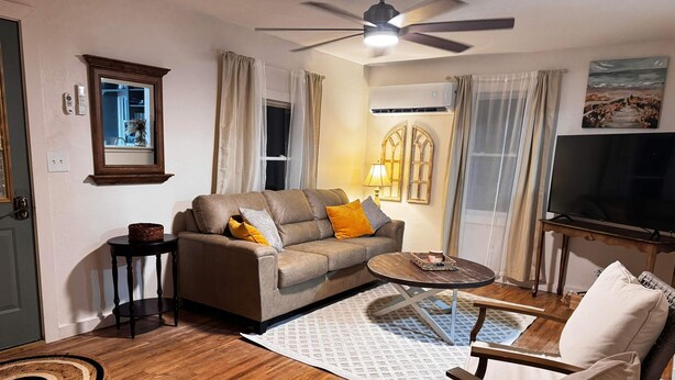 Uma sala de estar com sofá, poltrona, mesa de centro e ventilador de teto.