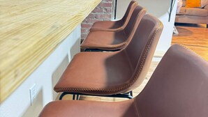 Uma área de estar com uma mesa de madeira e cadeiras marrons, uma máquina de café e uma parede com um letreiro com tema de café.