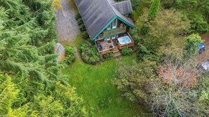 Eine Vogelperspektive zeigt eine Hütte mit Terrasse und Whirlpool, umgeben von dichtem Wald.