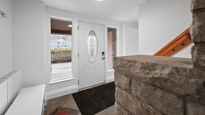 A white interior with a stone wall, a white door with a glass panel, and a wooden staircase.