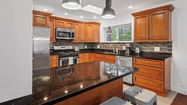 A modern kitchen with wooden cabinets, a granite countertop, stainless steel appliances, and pendant lighting.