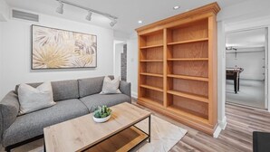 A modern living room with a grey sofa, a wooden coffee table, and a large wooden bookshelf.
