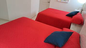 Two single beds with red bedding and dark blue pillows in a room with white walls and a door.