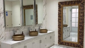Un baño con suelo de mármol, un tocador con tres lavabos y un espejo grande con marco ornamentado.