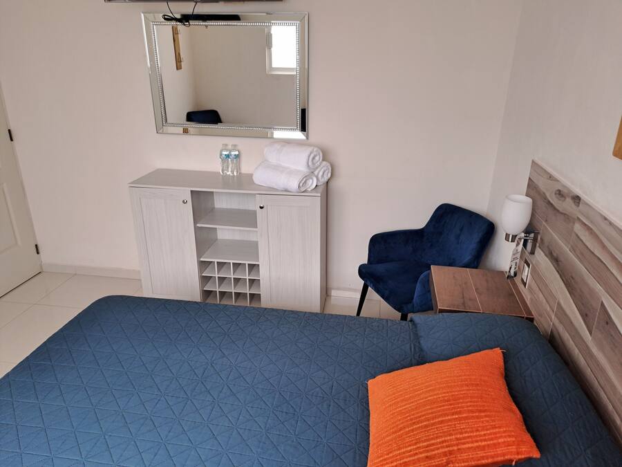 A bedroom with a bed, a blue chair, a wooden cabinet, and a mirror.