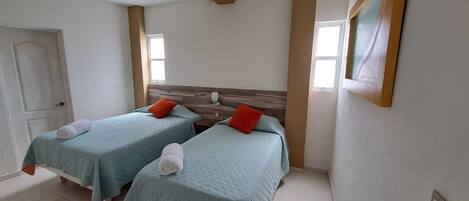 A hotel room with two beds, a wooden headboard, a white door, and a framed picture on the wall.