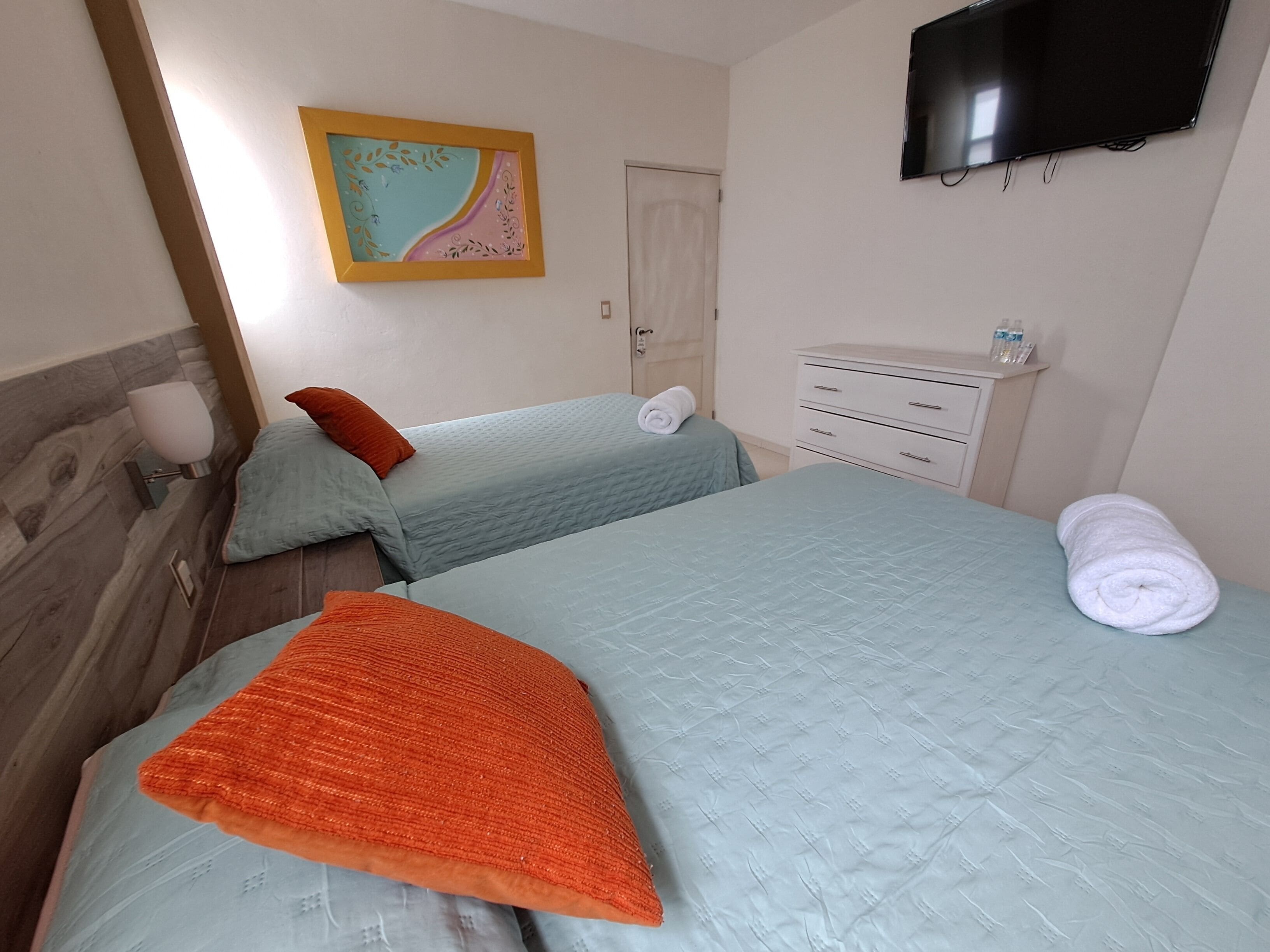 A bedroom with two beds, a TV, a bedside table, and a wall-mounted artwork.