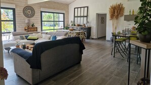 A spacious living room with a large sofa, a dining area with a table and chairs, and a kitchen area with a hanging plant.