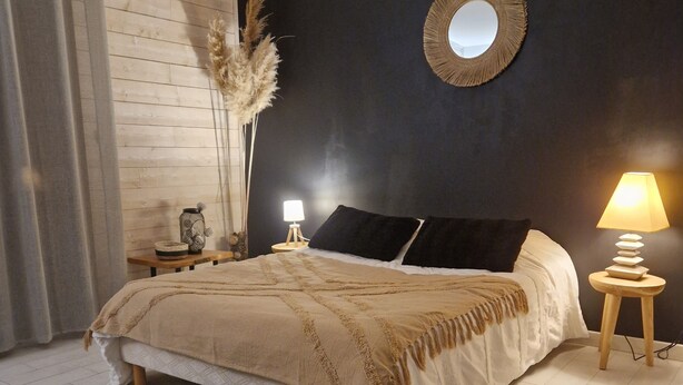 A bedroom with a bed, two bedside tables, a mirror, a lamp, a rug, and a basket.