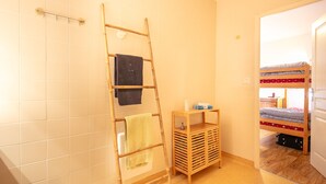 A bathroom with white tiled walls, a wooden ladder, a small wooden shelf with toiletries, and a bunk bed in the adjacent room. - Hermine - apt 6p, vue montagne (Chamrousse)