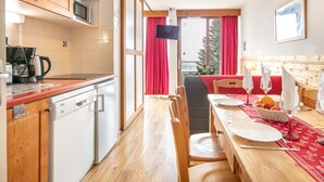 A kitchen with wooden cabinets, a dishwasher, and a dining area with a table set for two. - Hermine - apt 6p, vue montagne (Chamrousse)