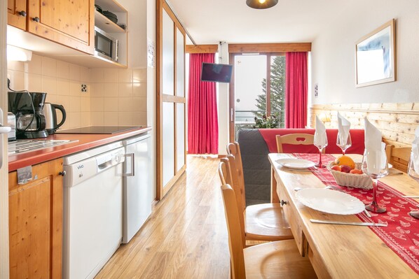 A kitchen with wooden cabinets, a dishwasher, and a dining area with a table set for two. - Hermine - apt 6p, vue montagne (Chamrousse)