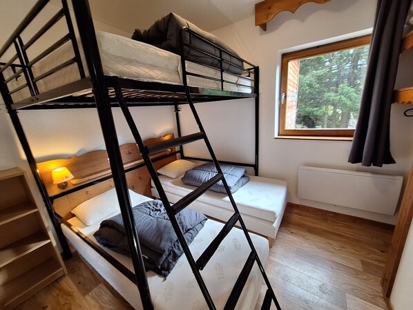 Een slaapkamer met een stapelbed, een raam, een radiator en een houten vloer.