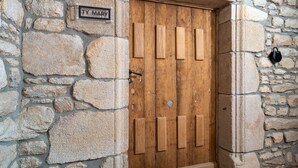 Un muro de piedra con una puerta de madera, una placa con el nombre 'TY MARY' y un objeto negro en la pared.