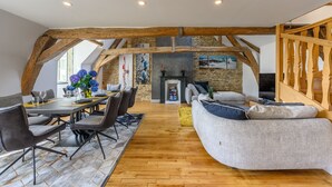 Una habitación amplia con vigas de madera a la vista, una chimenea de piedra y una zona de estar acogedora con sofá y sillones.