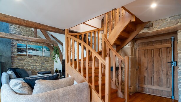 Un espacio de sala acogedor con escalera de madera, pared de piedra y vista al océano.