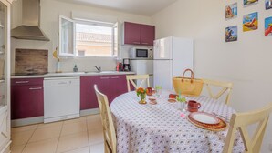 Cocina compacta equipada con lavavajillas, microondas y refrigerador. Una mesa de comedor con sillas dispuesta con un mantel individual, una cesta y un florero.