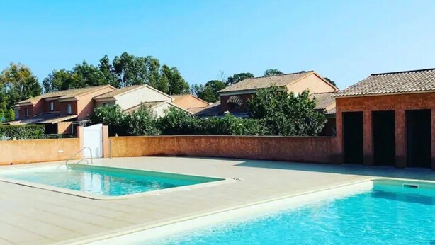 Una piscina con dos zonas separadas, rodeada por un muro de ladrillo bajo y un cielo azul despejado.