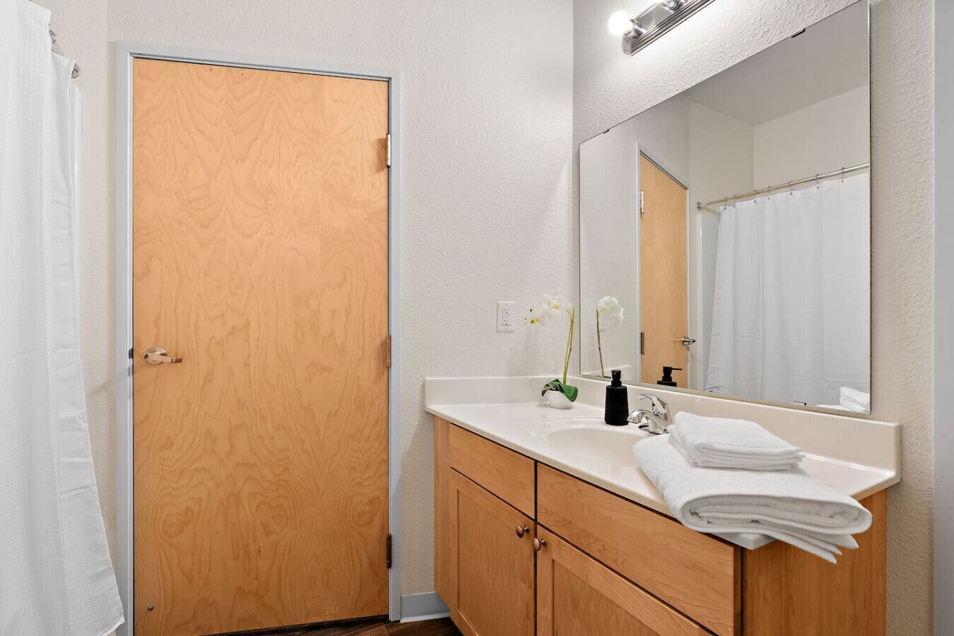 A bathroom with a wooden door, a white sink with a mirror, and a towel rack.