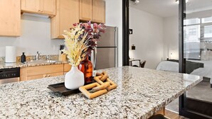 A modern kitchen with granite countertops, wooden cabinets, and a glass door leading to a bedroom.