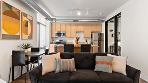 A modern living room with a dark brown sectional sofa, a dining table with chairs, and a kitchen in the background.